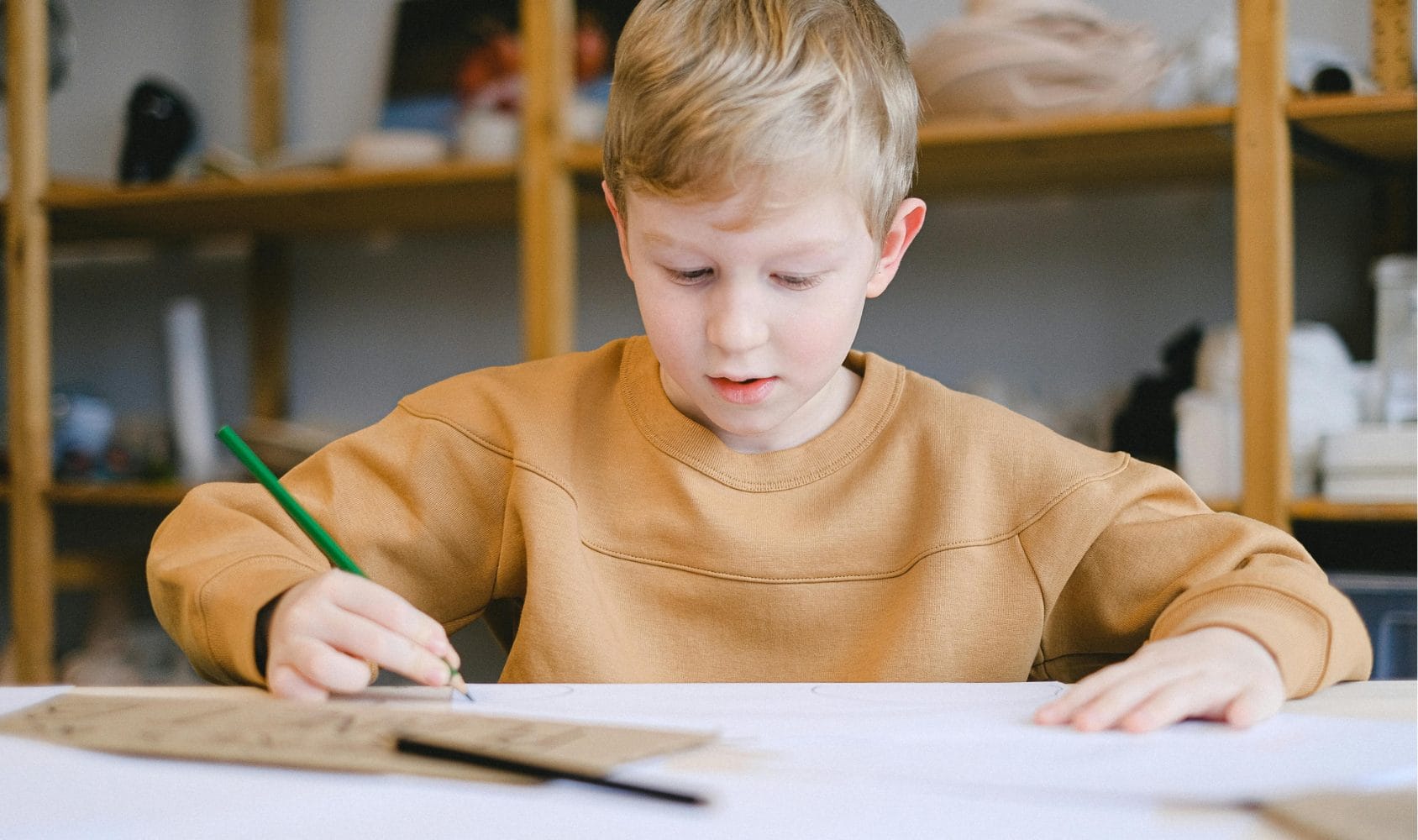 Boy sat at table drawing.