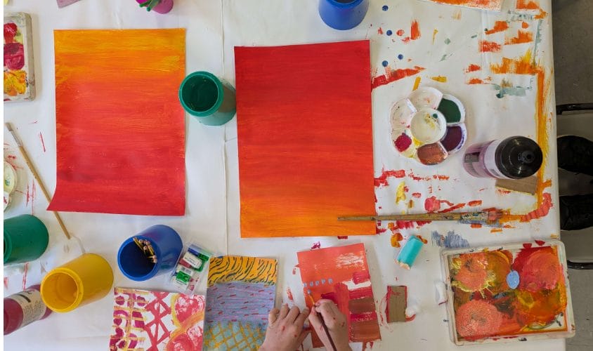 Table in an art studio with lots of paintings on it.