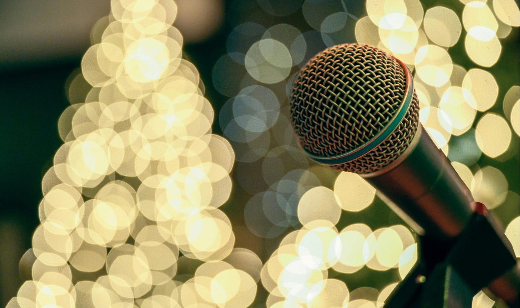 Photo of a Microphone in front of a lit up Christmas tree.
